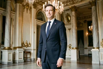 Portrait officiel d'un homme politique en costume sombre dans un hall présidentiel aux dorures classiques, illustrant le protocole officiel de l'Élysée